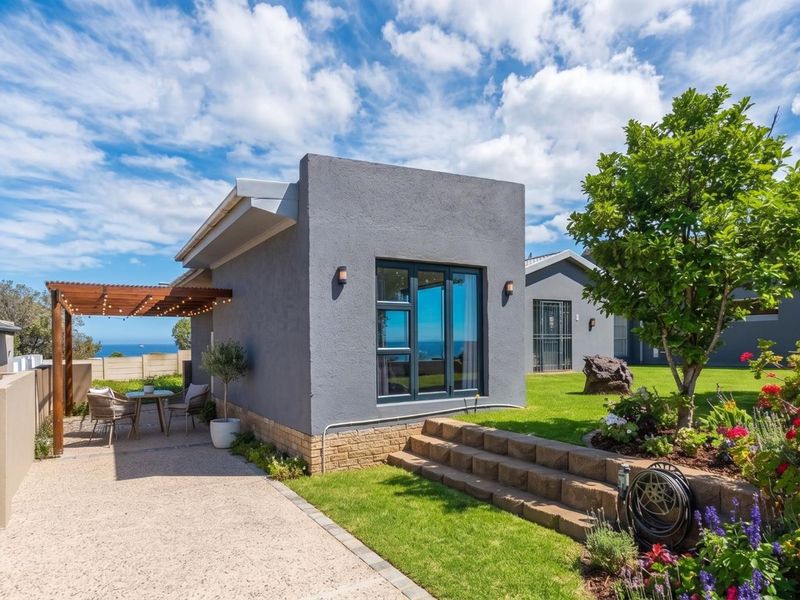 A well-maintained rear exterior featuring a modern grey facade, timber pergola over a paved patio, and a landscaped garden with stone retaining walls.