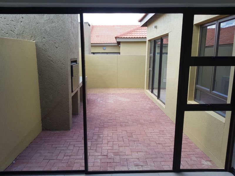 A private paved patio area featuring a built-in braai, enclosed by boundary walls and accessible via sliding glass doors.