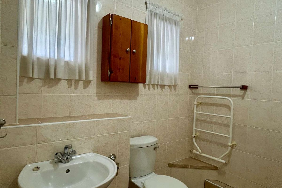 A functional bathroom featuring tiled walls, a pedestal basin, a toilet, and a wall-mounted heated towel rail.