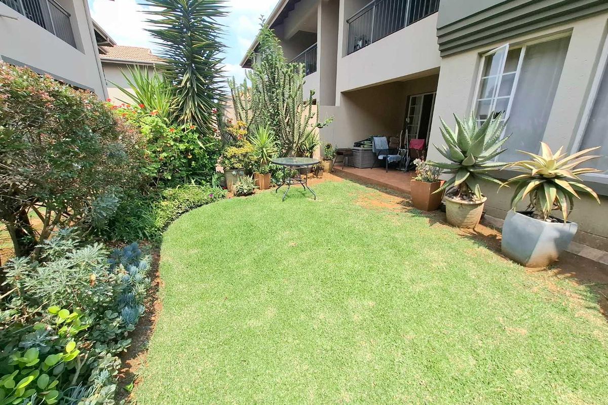 A private rear garden area featuring a small lawn, established succulent landscaping, and a covered patio space attached to the townhouse structure.