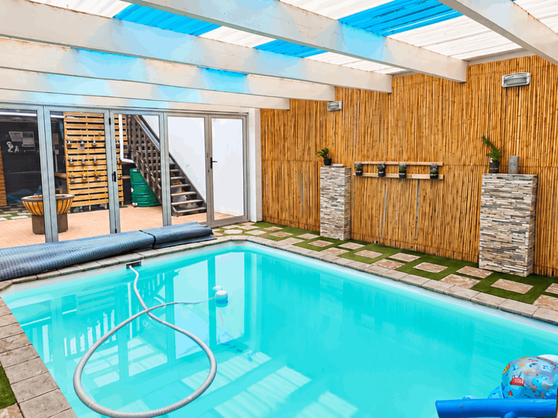 A well-maintained covered pool area featuring bamboo wall cladding, stone accents, and folding glass doors leading to an adjacent outdoor space.