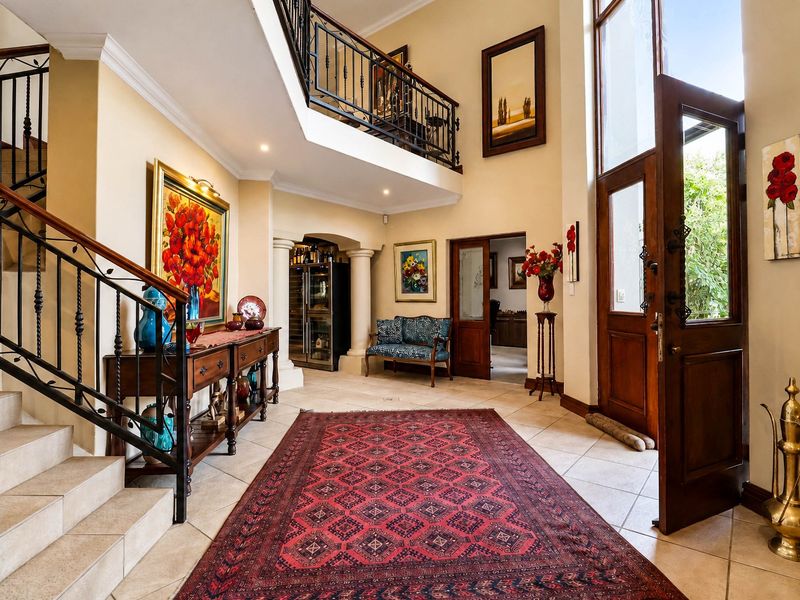 Grand double-volume entrance hall featuring tiled flooring, a striking wrought iron staircase, and an integrated wine cellar area.