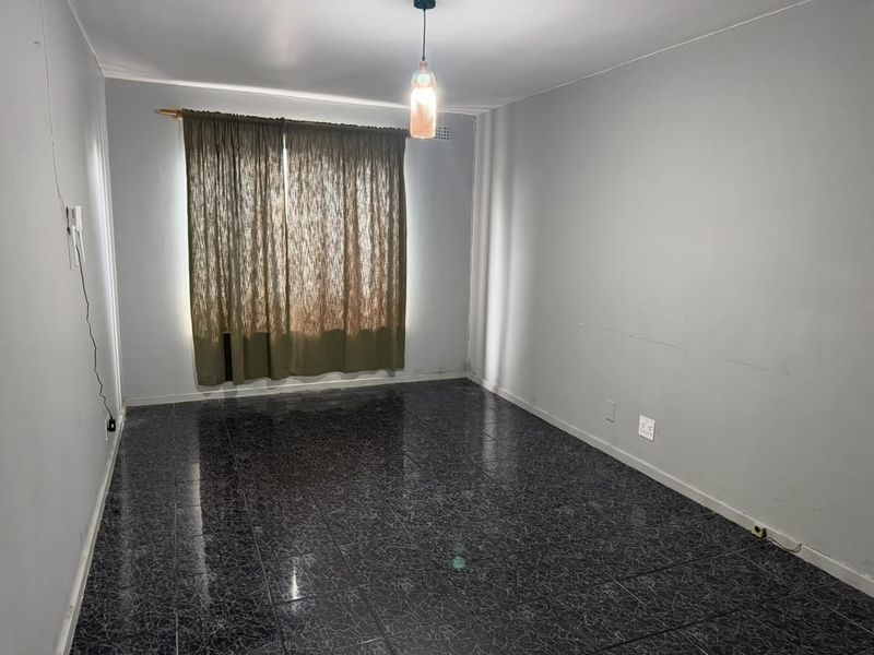 An empty living room featuring dark tiled flooring and neutral walls, providing a blank canvas for interior design and personalization.