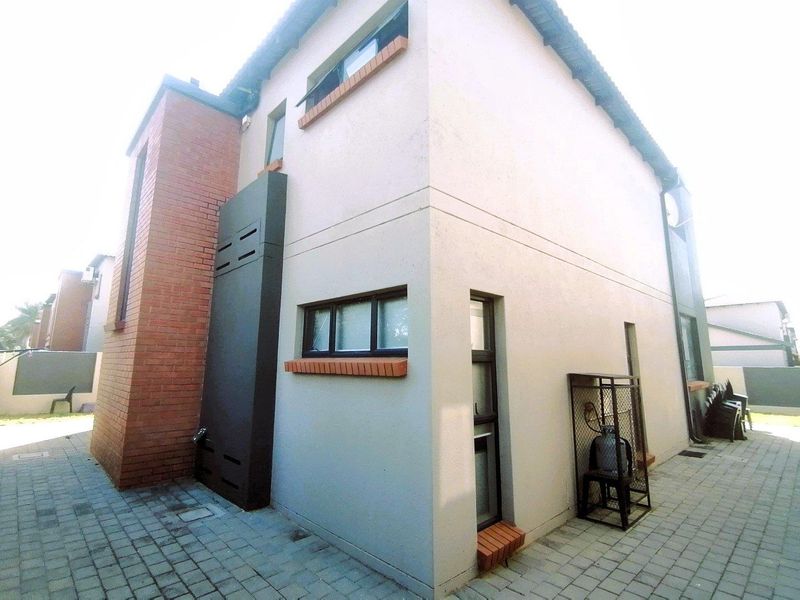 Rear exterior view of the townhouse featuring a paved courtyard, brick and plastered wall finishes, and secure gas cylinder storage.
