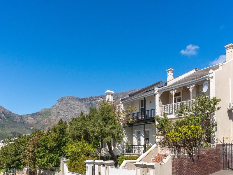 A charming double-story residential property featuring a classic balcony, brick boundary wall, and mountain views in a scenic neighborhood setting.