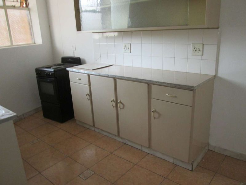 A functional kitchen featuring tiled flooring, a tiled backsplash, laminate countertops, and built-in cabinetry with a freestanding stove.
