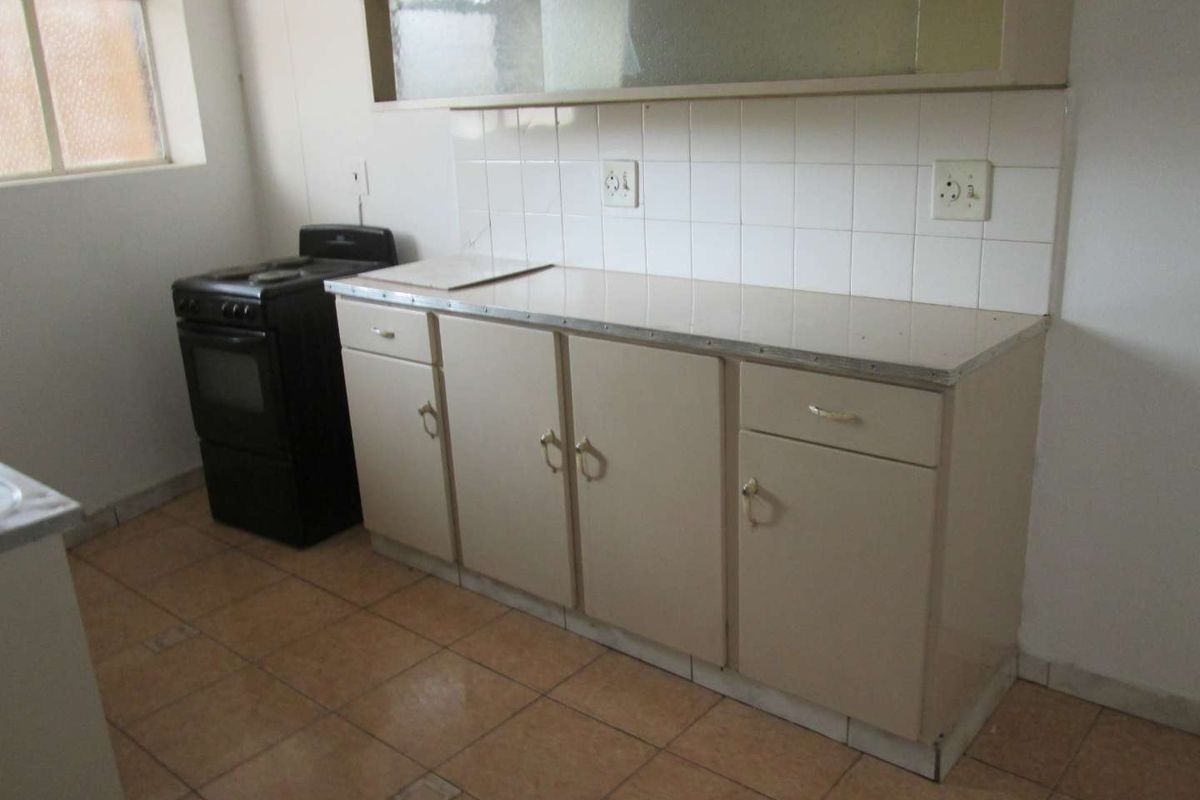 A functional kitchen featuring tiled flooring, a tiled backsplash, laminate countertops, and built-in cabinetry with a freestanding stove.