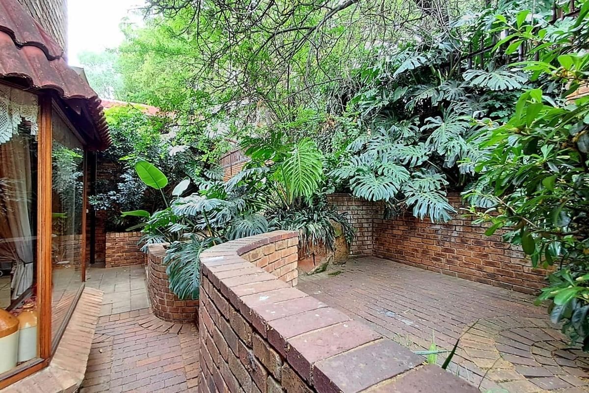 A private rear garden area featuring brick paved flooring, low brick retaining walls, and established lush greenery.