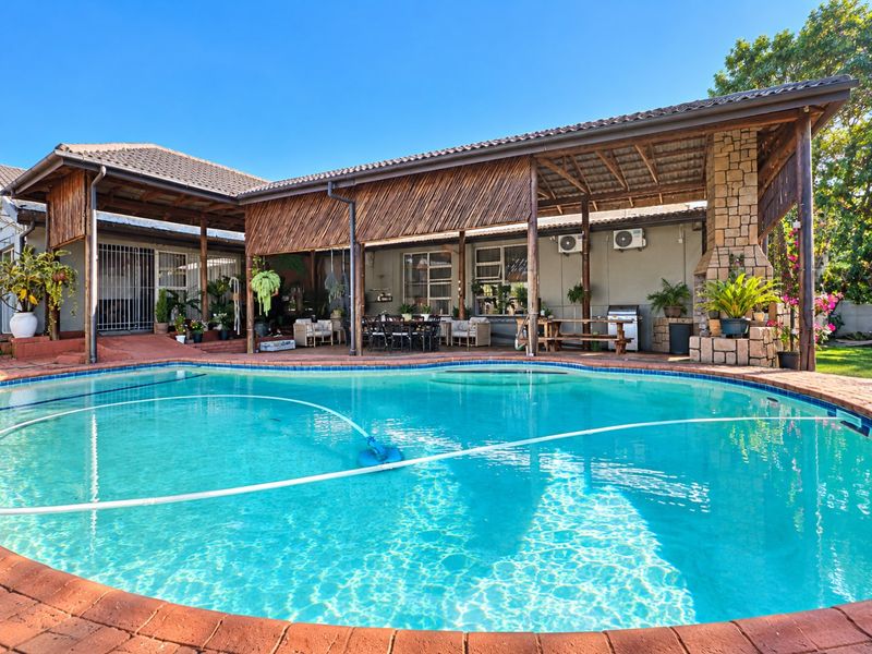 Spacious outdoor entertainment area featuring a large swimming pool, covered patio with a stone fireplace, and well-maintained brick paving.
