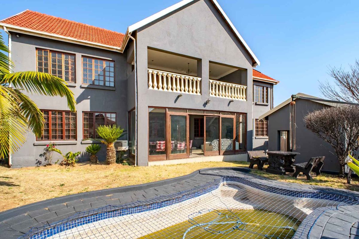 Rear view of a two-story house featuring a swimming pool with safety net, a covered balcony, and sliding glass doors leading to the interior.