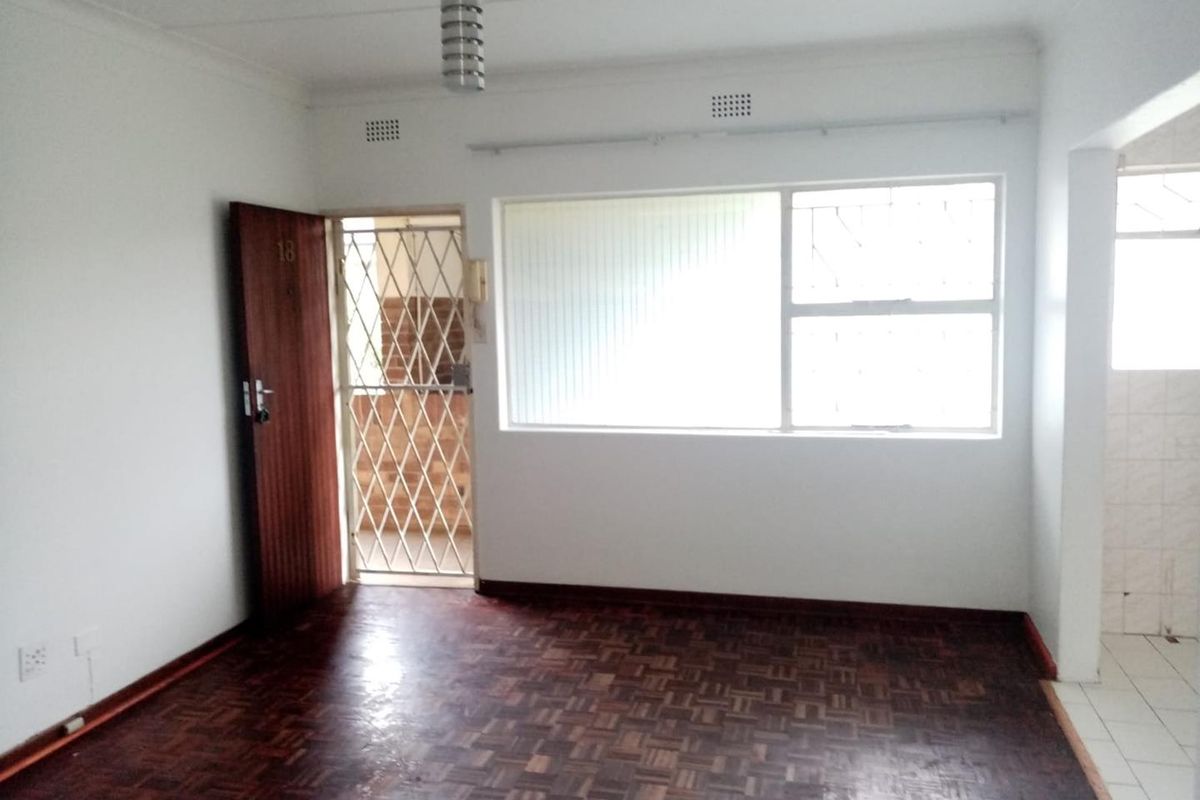 An empty living area featuring classic parquet flooring, a secure entrance gate, and large windows providing natural light.