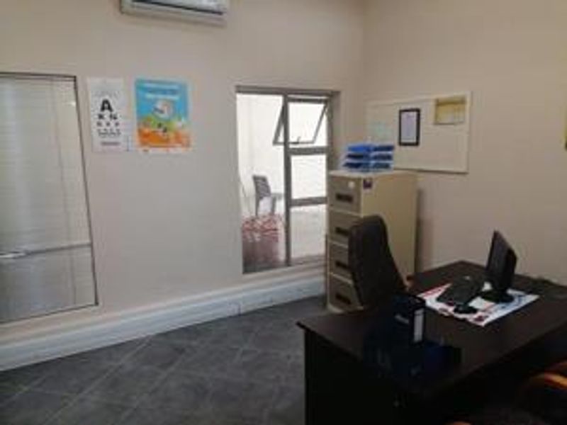 A functional office space featuring tiled flooring, aluminium window frames, and a wall-mounted air conditioning unit.