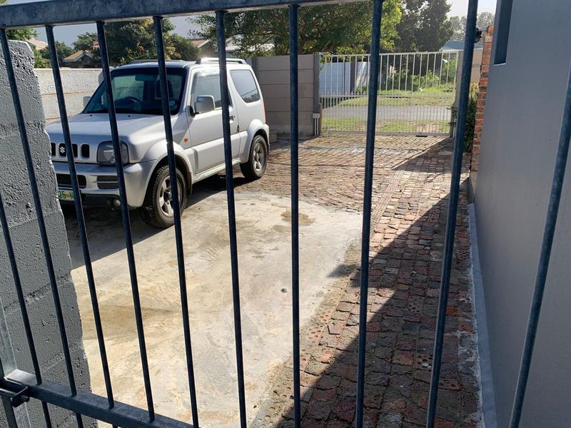 Front entrance area featuring a metal security gate, a combination of brick paving and concrete driveway, and perimeter walling.