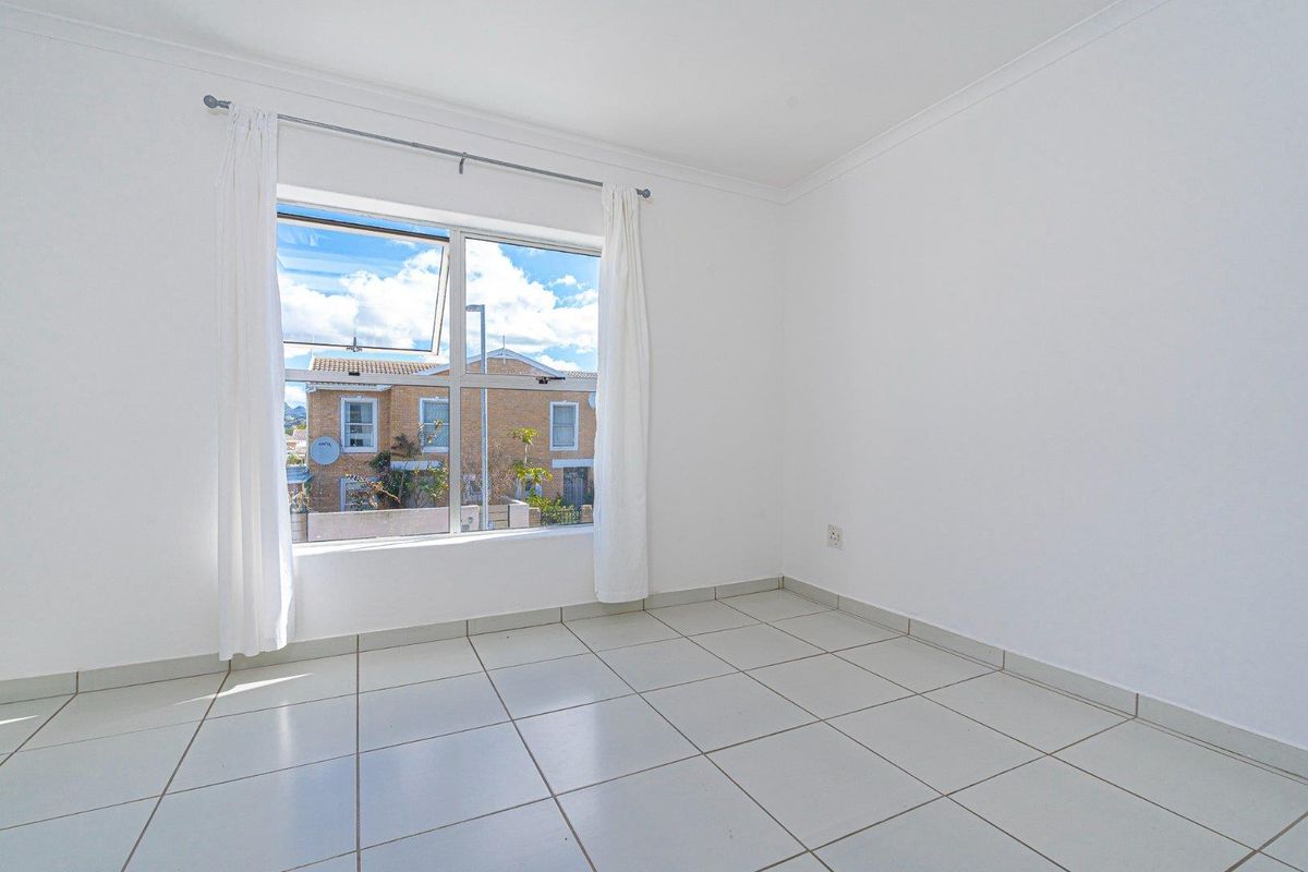 A bright, empty bedroom featuring neutral tiled flooring, white walls, and a large window providing natural light and a view of the neighborhood.