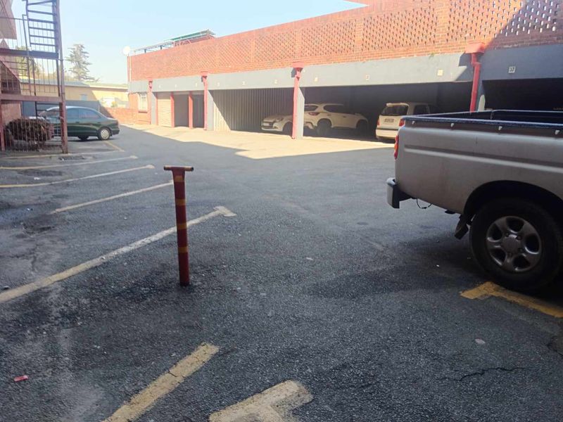 An outdoor parking area featuring multiple covered parking bays with a brick facade and asphalt driveway.