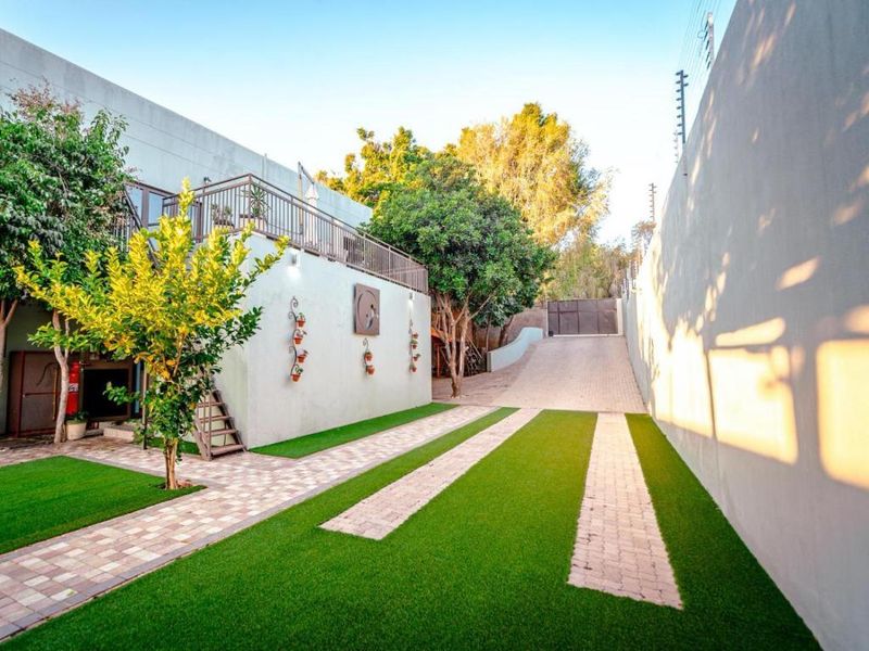 A well-maintained front exterior featuring a paved driveway, artificial turf landscaping, and an elevated balcony area with secure perimeter walls.