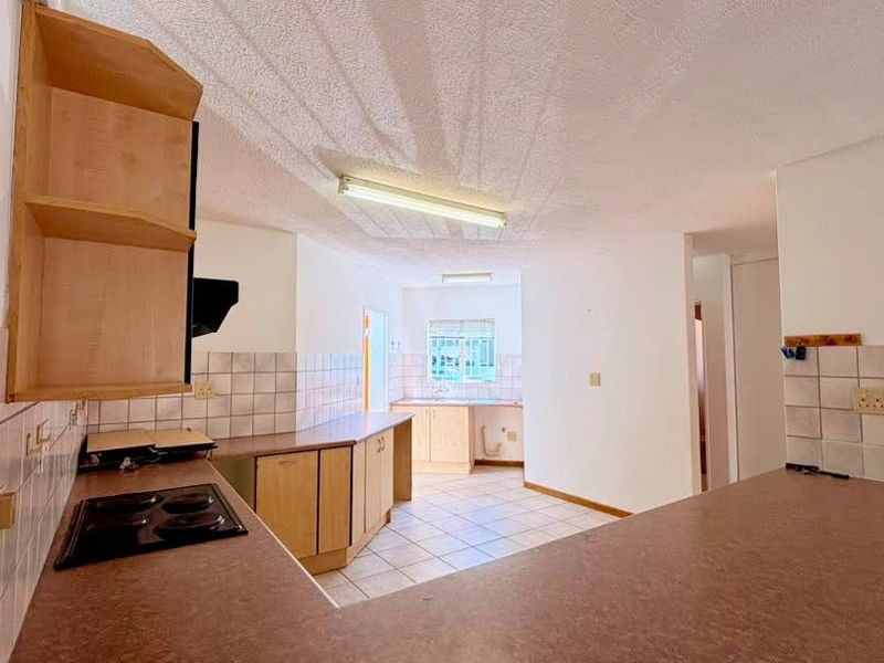 A functional kitchen space featuring built-in cabinetry, laminate countertops, an electric hob, and tiled backsplash, offering a blank canvas for modern renovation.