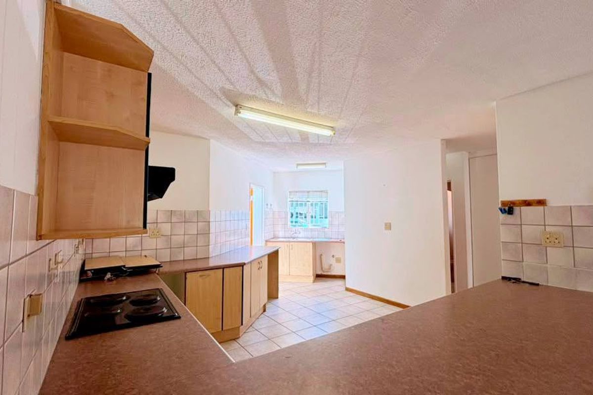 A functional kitchen space featuring built-in cabinetry, laminate countertops, an electric hob, and tiled backsplash, offering a blank canvas for modern renovation.