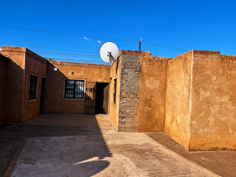 Rear exterior view of the property featuring a concrete patio area, security gates, and satellite dish mounted on the brick wall.