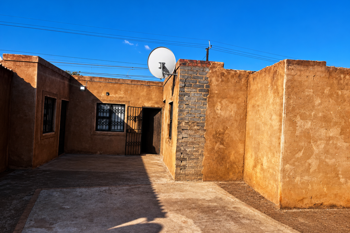 Rear exterior view of the property featuring a concrete patio area, security gates, and satellite dish mounted on the brick wall.