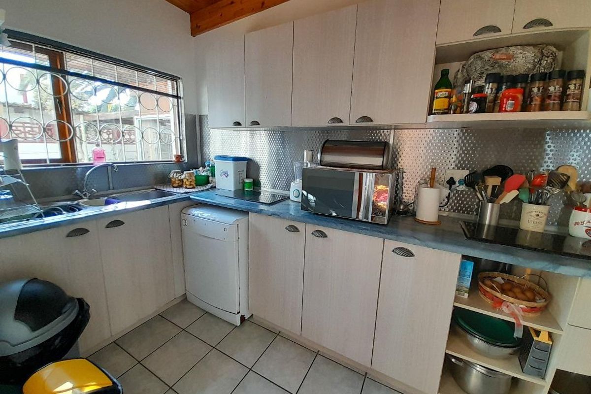 Functional kitchen featuring light-toned cabinetry, stainless steel backsplash, tiled flooring, and exposed timber ceiling beams, providing a practical workspace.
