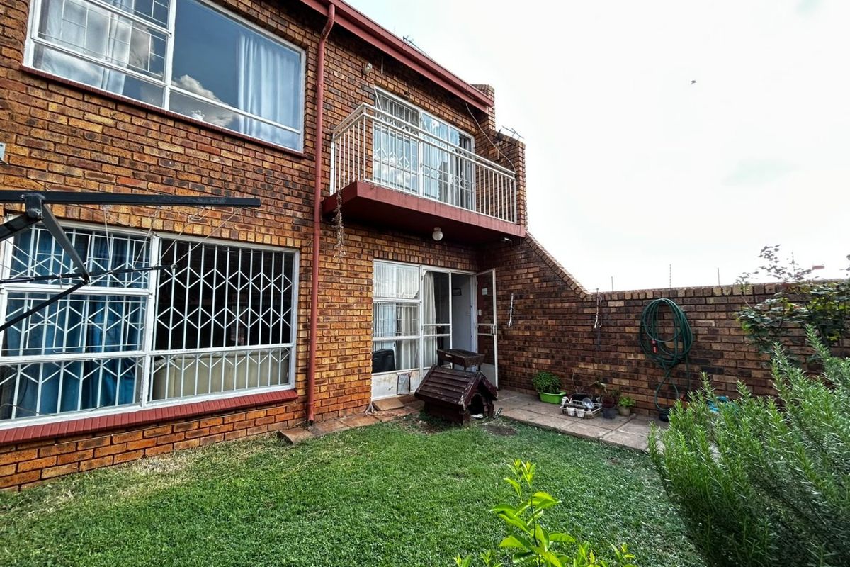 Rear view of the townhouse featuring a brick facade, a small balcony, a paved patio area, and a private garden space.