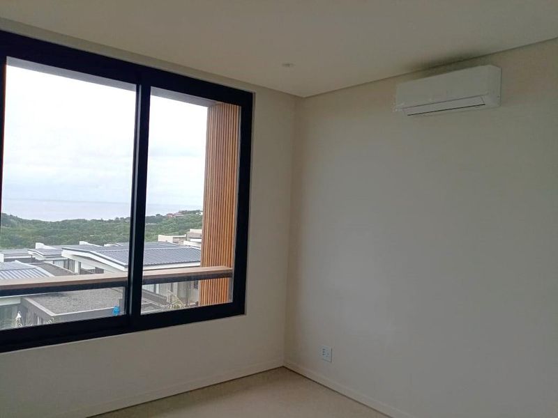 A bright, modern bedroom featuring neutral carpet, a wall-mounted air conditioning unit, and a large sliding door with scenic views.