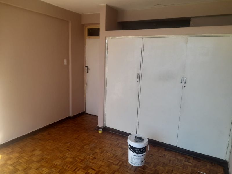 An empty bedroom featuring original parquet flooring and built-in storage cupboards, presenting a blank canvas for renovation or interior design updates.
