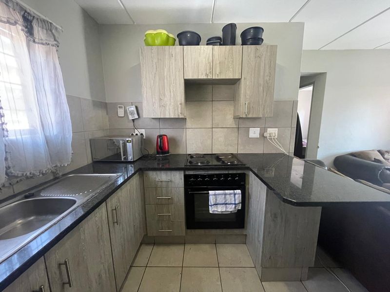 A functional kitchen featuring light wood-look laminate cabinetry, dark granite countertops, a built-in oven with electric hob, and neutral tiled splashbacks.