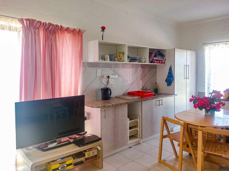 Open-plan living area featuring a compact kitchenette with granite countertops, marble-effect splashback, and tiled flooring throughout.