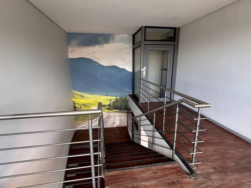 Modern office hallway featuring a staircase with stainless steel balustrades and a built-in elevator, finished with durable laminate flooring.