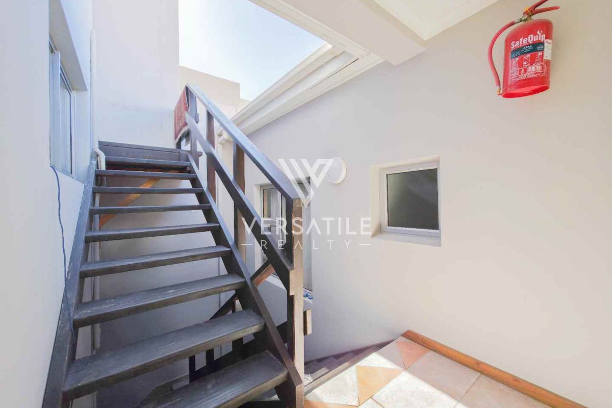 An outdoor staircase area featuring a wooden staircase, tiled flooring, and a wall-mounted fire extinguisher.