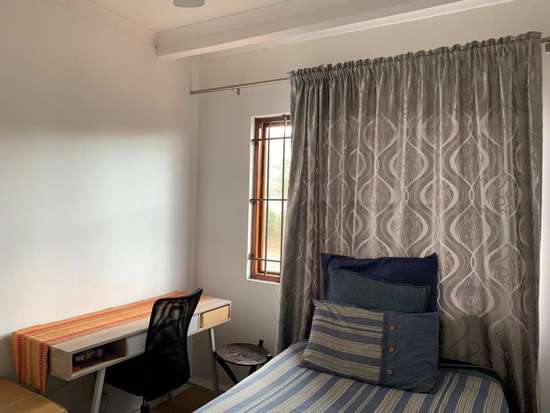 A functional bedroom featuring a window with security bars and a curtain rod, providing natural light and basic security.