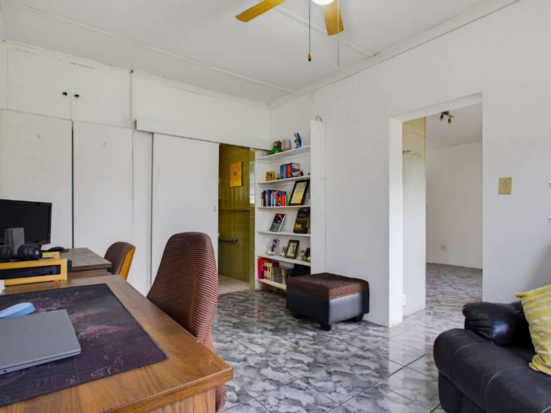 A living area featuring tiled flooring, a ceiling fan, and built-in storage cupboards, offering a functional space with potential for modernization.
