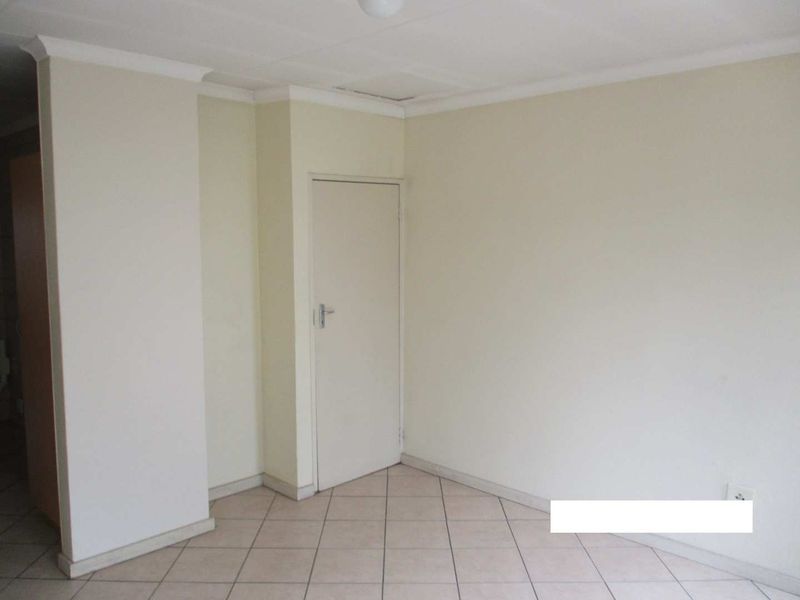 An empty living area featuring neutral wall paint, tiled flooring, and classic cove cornicing, providing a clean and versatile space.