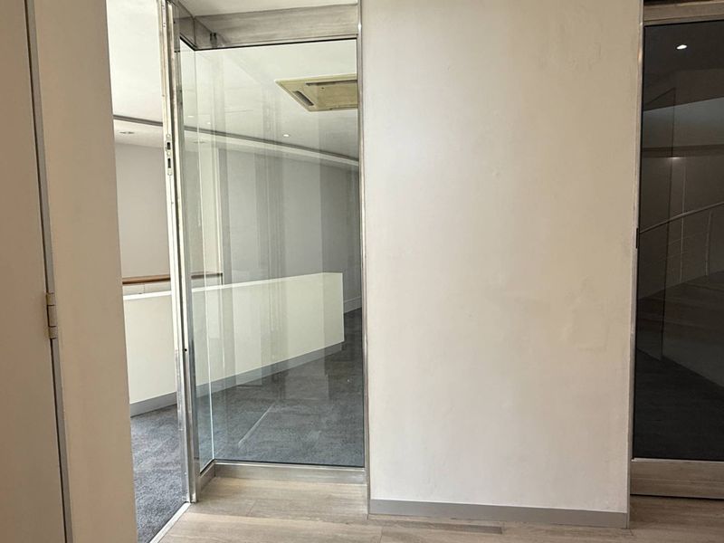 An empty office space featuring glass partitions, recessed ceiling air conditioning, and carpet flooring, offering a clean and professional environment.