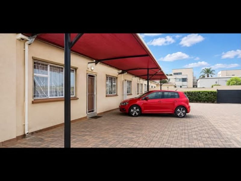 Exterior view of the townhouse front featuring a paved driveway and a covered carport area with security features on windows and doors.