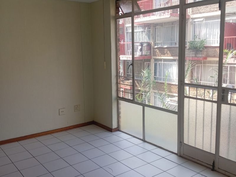 An empty, sunlit living area featuring tiled flooring and large windows with access to a balcony, offering a blank canvas for renovation.