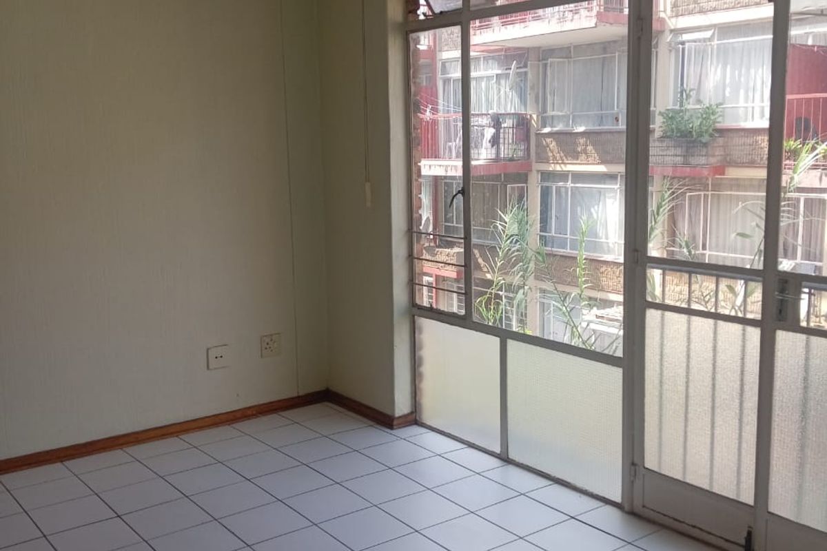 An empty, sunlit living area featuring tiled flooring and large windows with access to a balcony, offering a blank canvas for renovation.