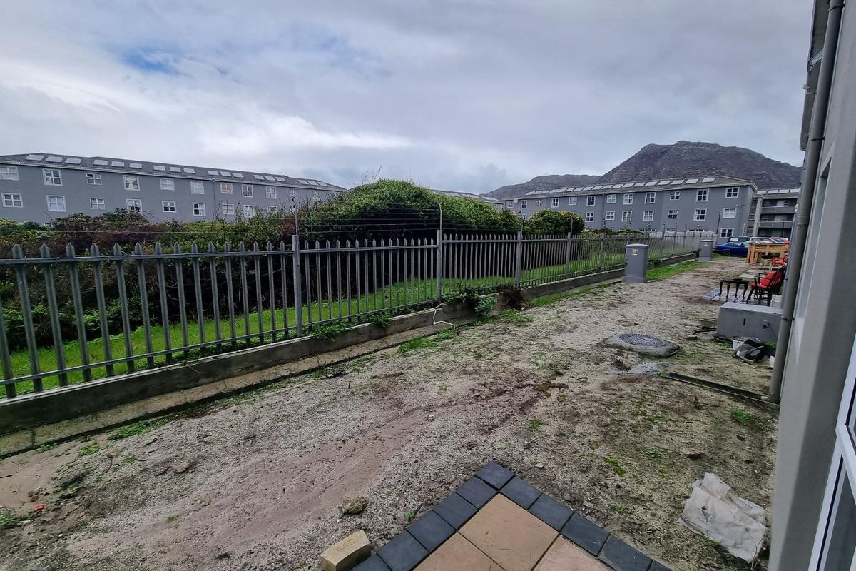Rear exterior area featuring a small paved patio section and an unlandscaped garden space enclosed by metal palisade fencing.
