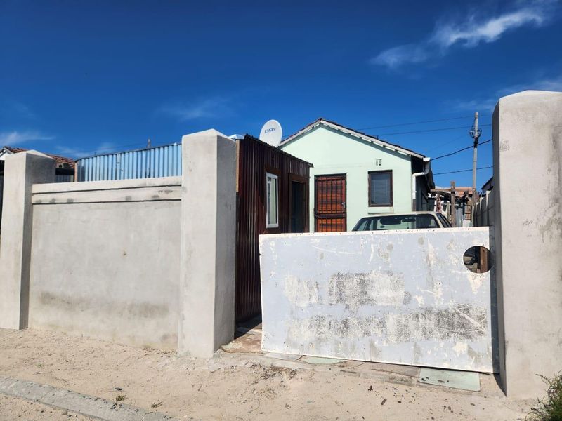 Front view of the property featuring a perimeter wall, security gate, and corrugated metal fencing with a satellite dish mounted on the roof.