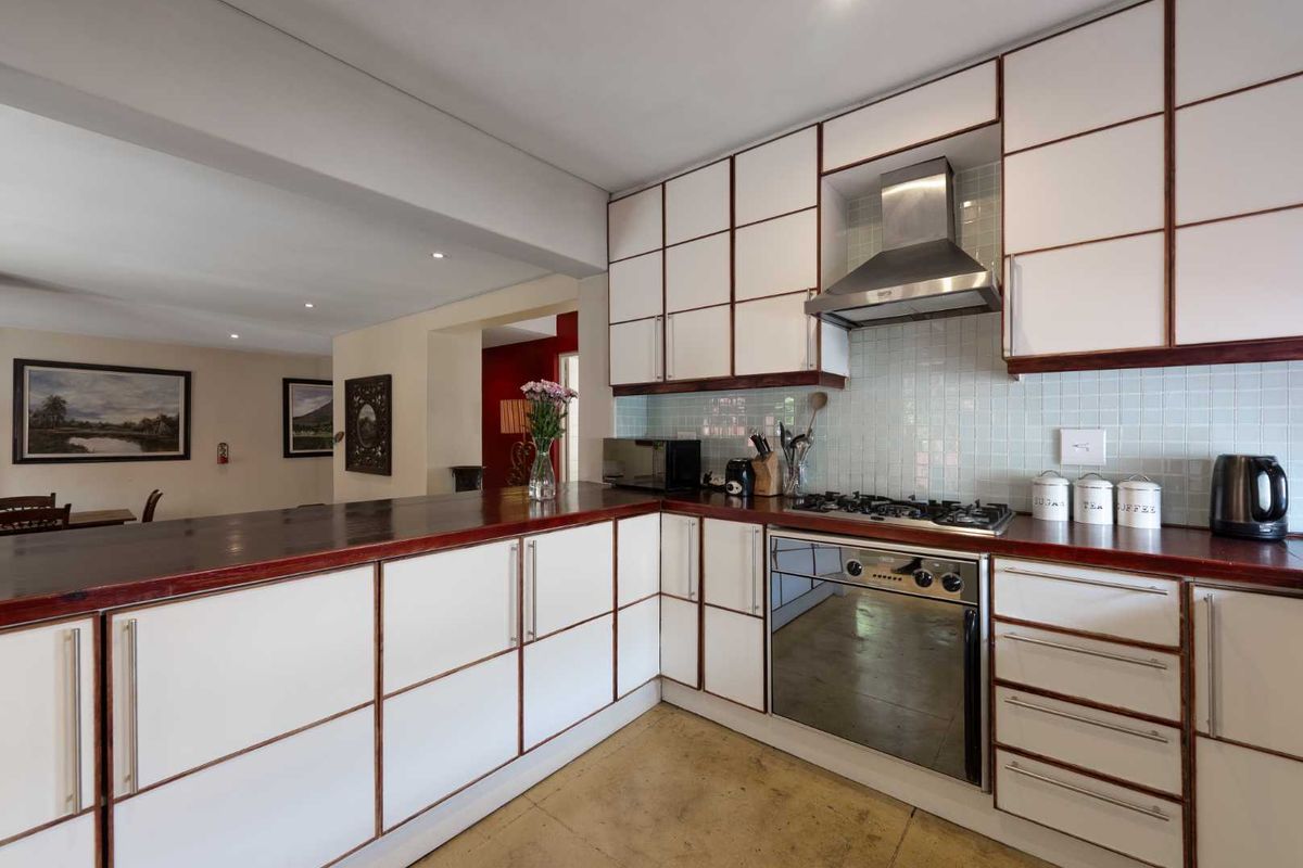 A functional kitchen featuring white cabinetry with dark wood trim, a gas hob, built-in oven, stainless steel extractor, and a breakfast bar counter.