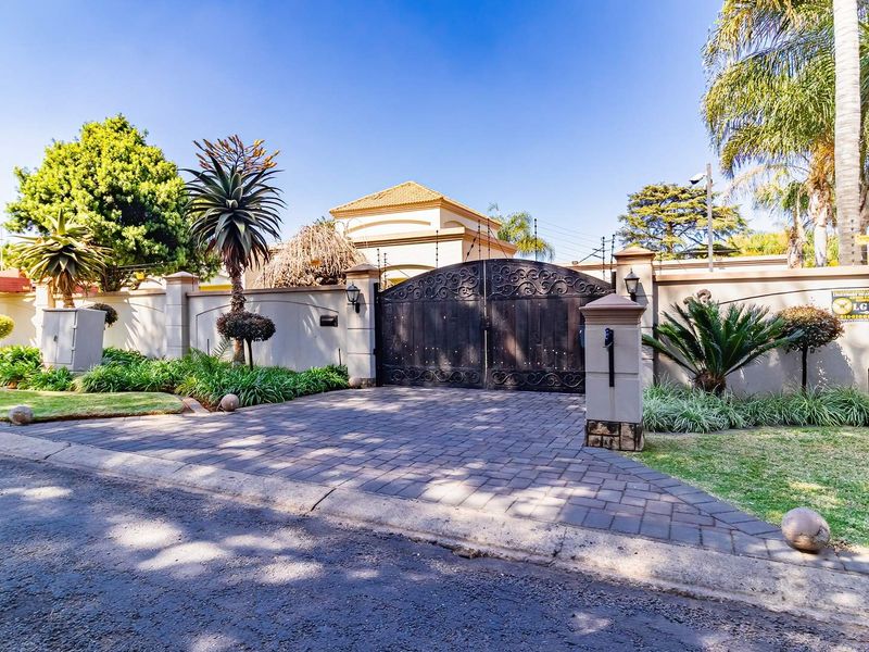 Front entrance view featuring a secure wrought iron gate, paved driveway, and perimeter wall with integrated electric fencing and pillar lighting.
