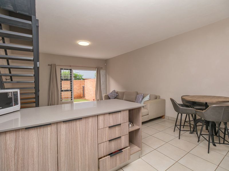 Open-plan living area featuring a modern kitchen island, tiled flooring, and a metal staircase leading to the upper level with access to the rear garden.