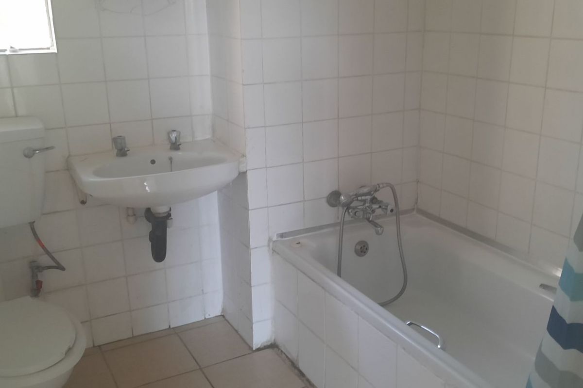 A dated bathroom featuring a standard bathtub, pedestal basin, and toilet with white wall tiling throughout.