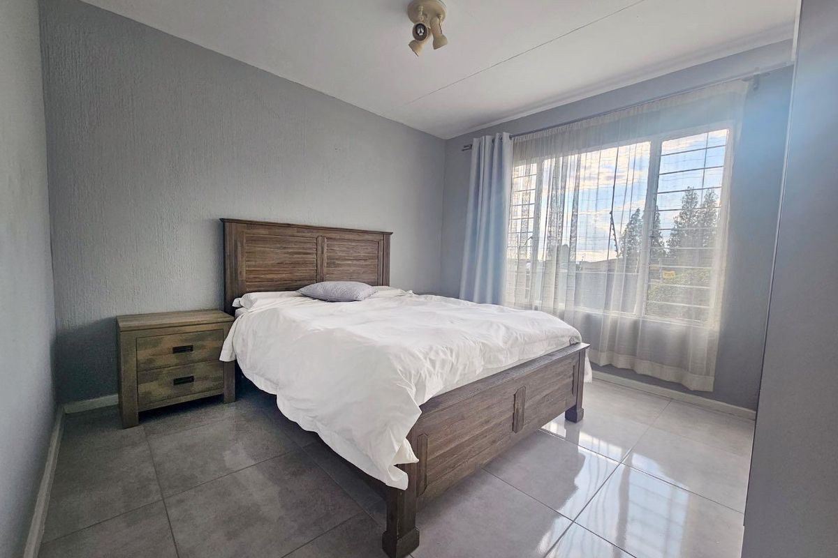 A bedroom featuring large format floor tiles, a window with security bars, and neutral grey wall finishes.
