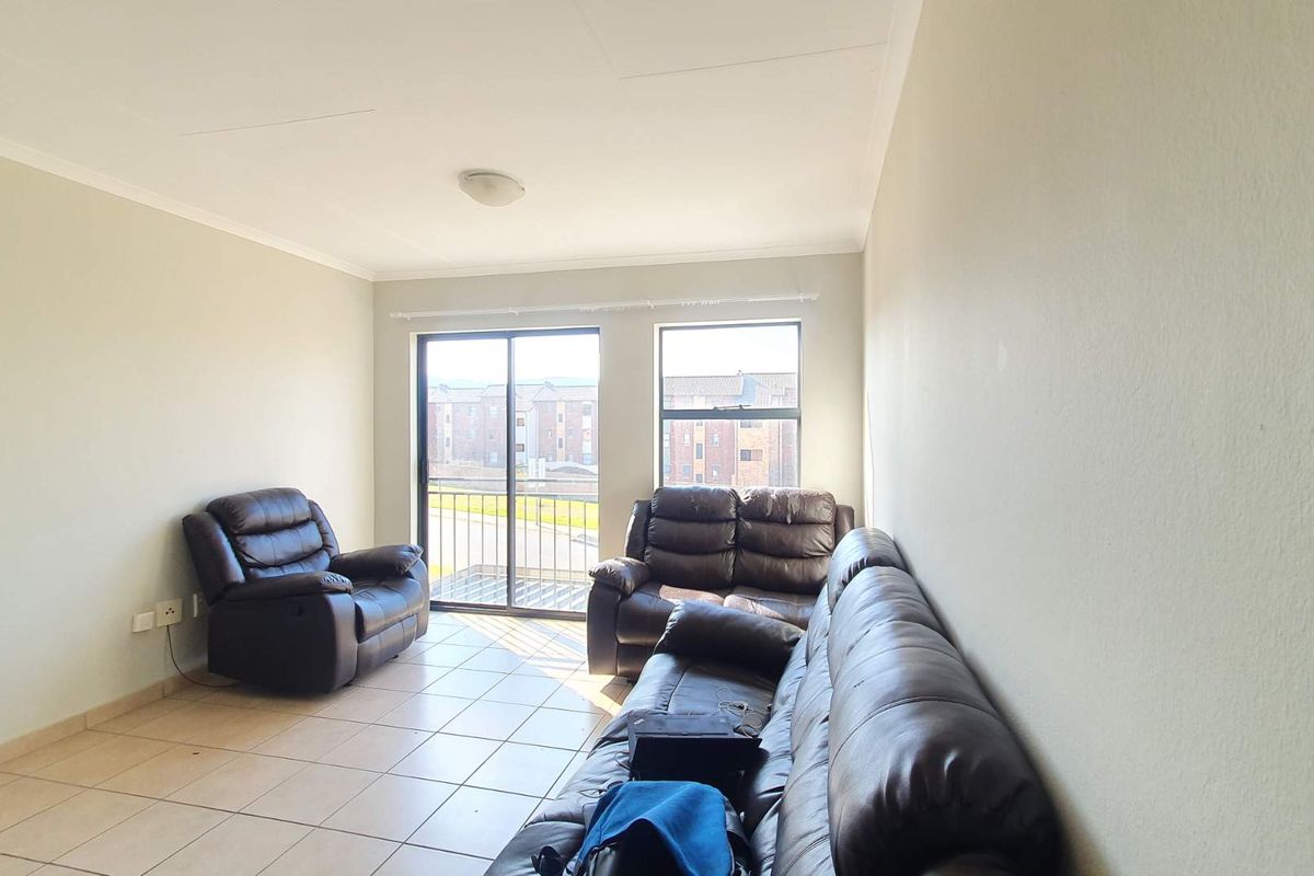 A living room featuring tiled flooring, a sliding glass door leading to a balcony, and large windows providing natural light.
