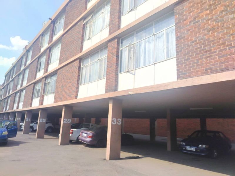 Exterior view of an apartment building featuring a brick facade and a ground-level covered parking area with numbered concrete support pillars.