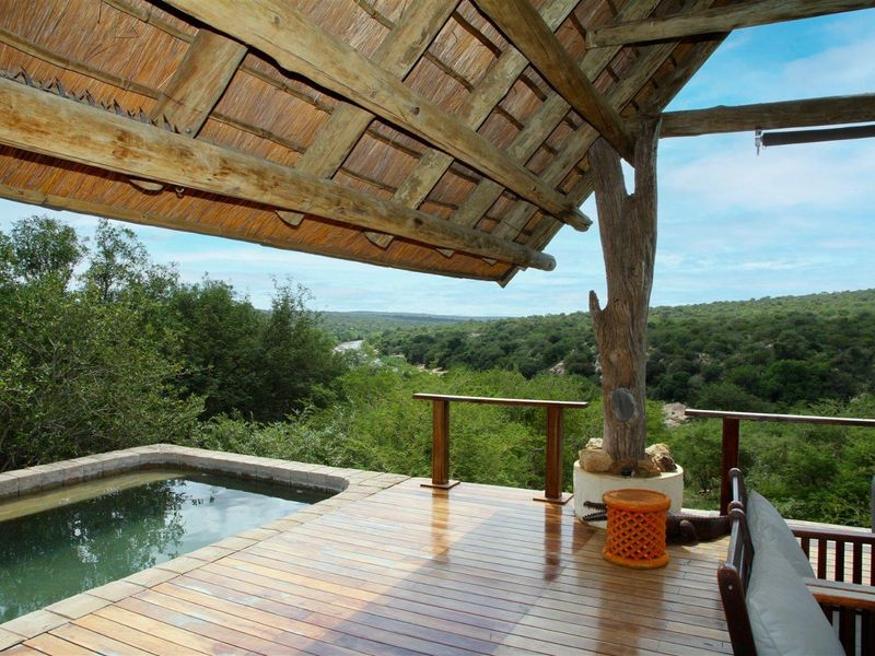 An elevated timber deck featuring a built-in plunge pool, covered by a traditional thatch roof, offering expansive views of the surrounding natural landscape.