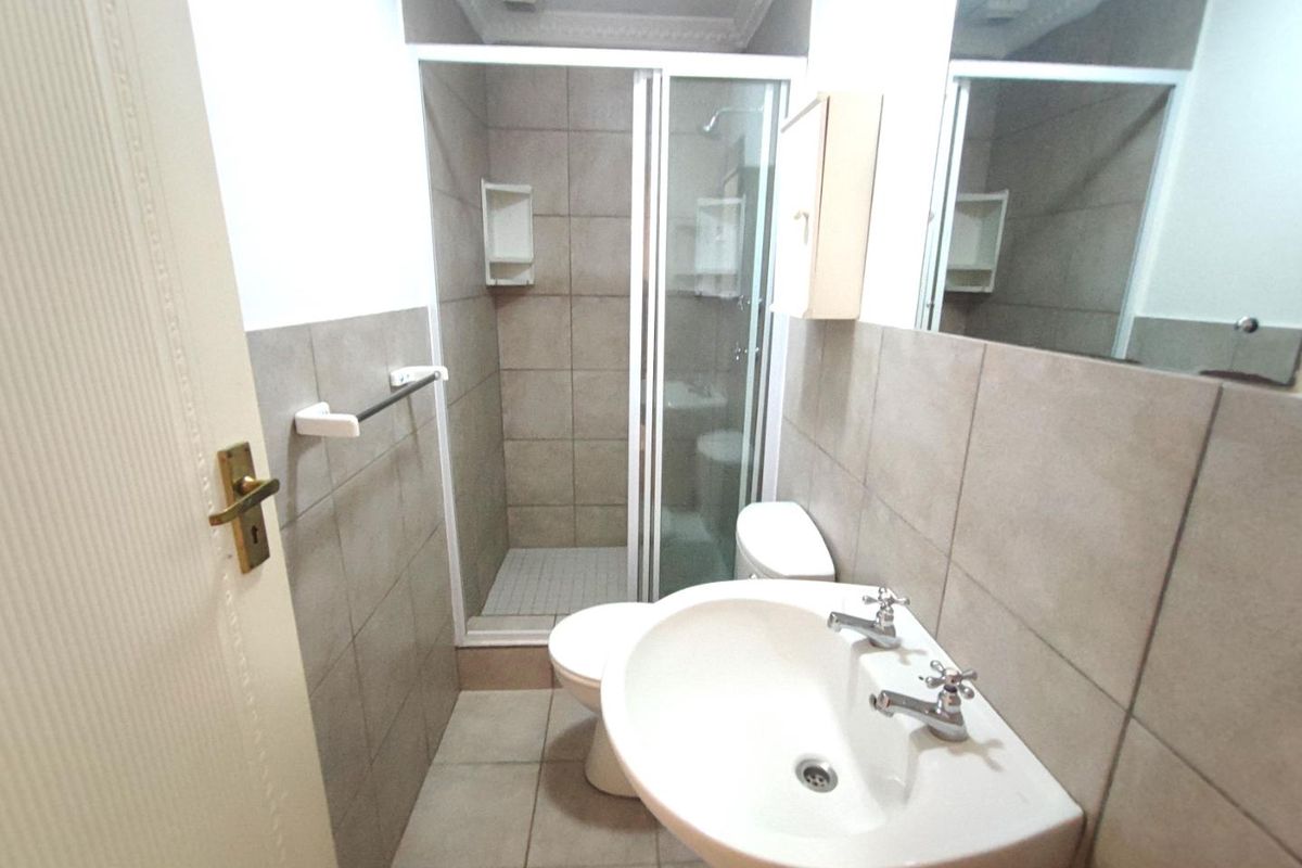 A functional bathroom featuring a shower enclosure, pedestal basin, toilet, and neutral wall and floor tiling.